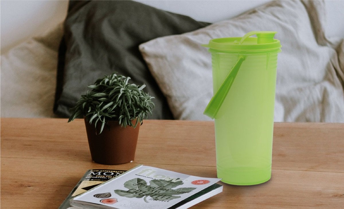 A translucent green Century tumbler on a wooden bedside table beside a magazine and a small plant